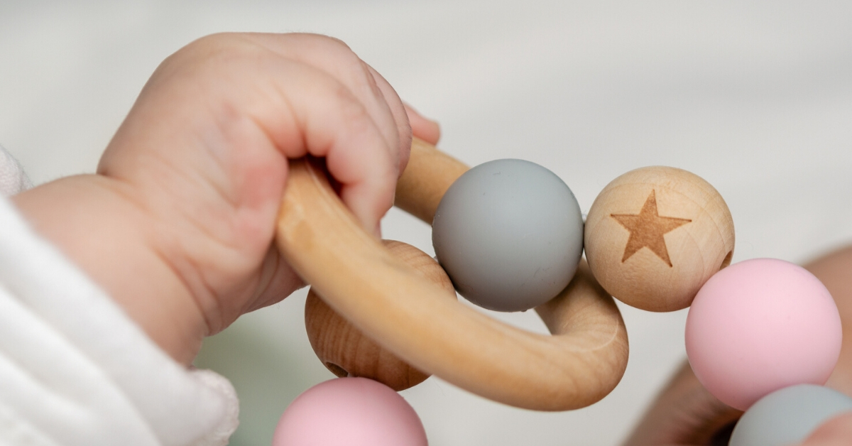 An infant’s hand holding on to a baby toy.