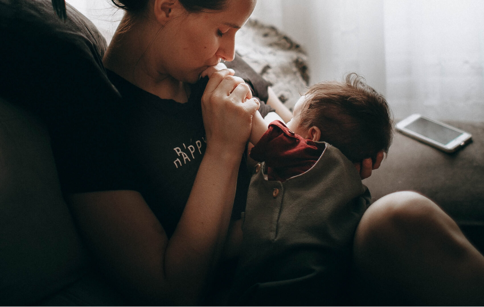 A parent breastfeeding a baby while gently kissing the baby's hand.