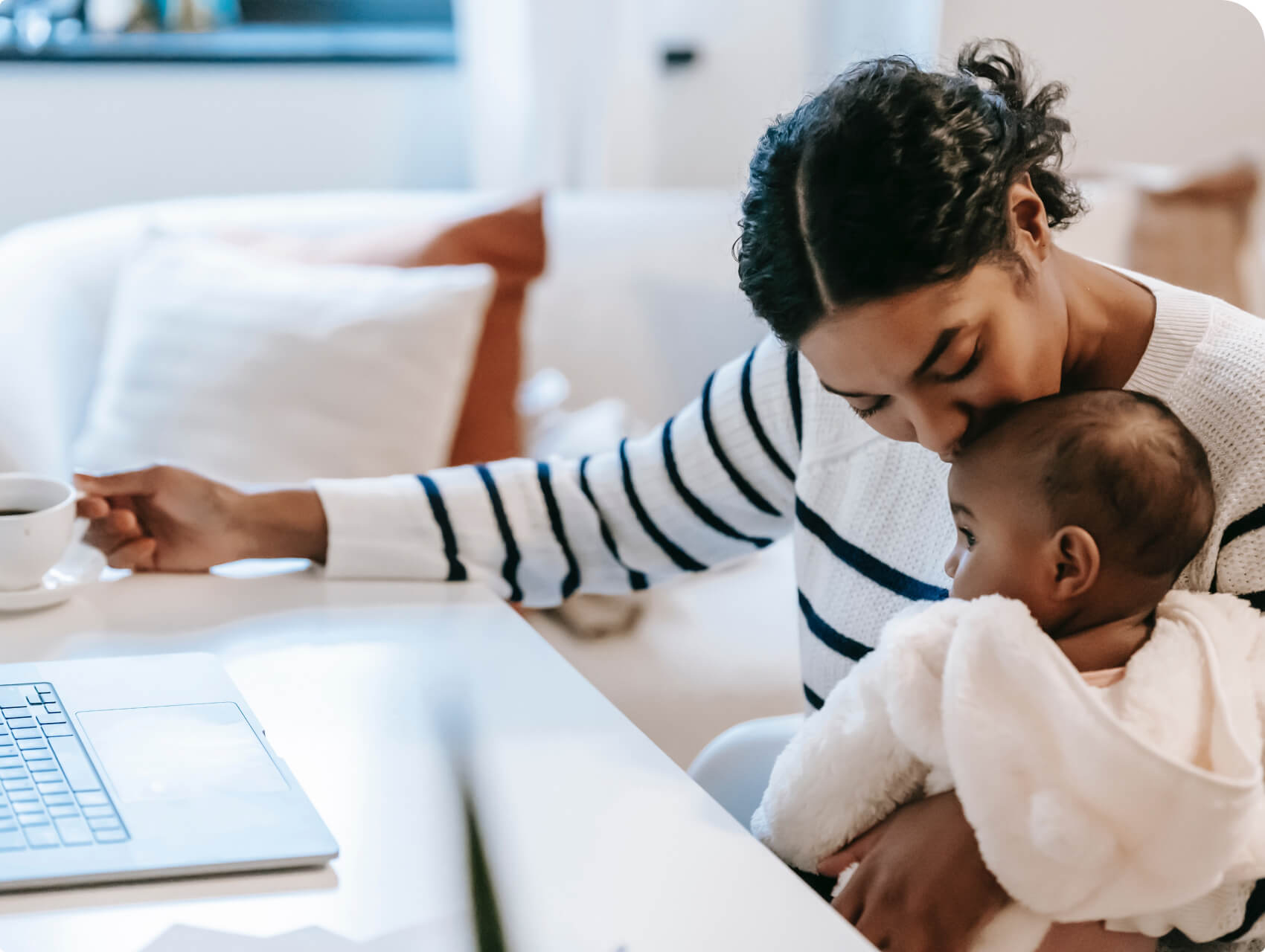 A parent kissing their baby on the forehead while working from home.