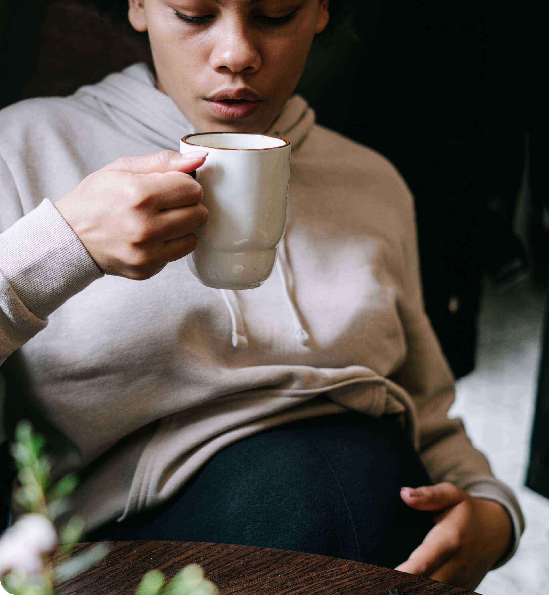 A parent sips on a hot beverage while cradling their belly.