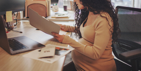 Pregnant woman working at a desk, balancing work and pregnancy, preparing for maternity leave.