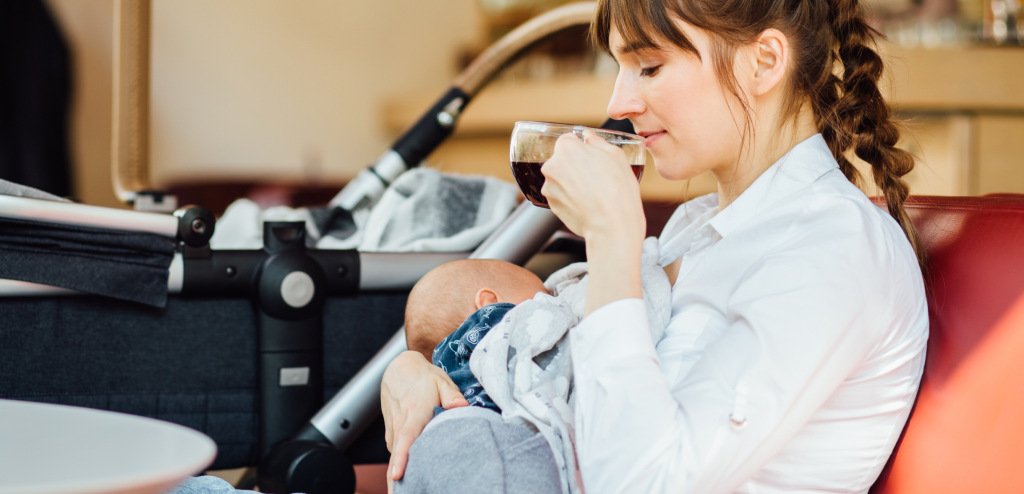 A young mother is breastfeeding her baby in a cafe while she is having a tea time